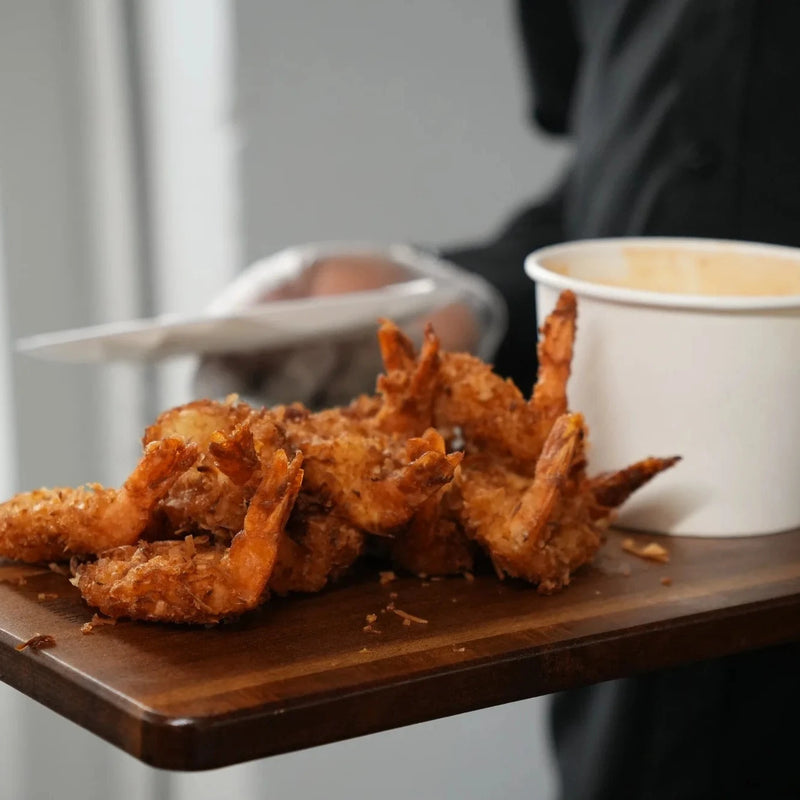 Fried shrimp on a wooden board with a white cup, held by a person in gloves.